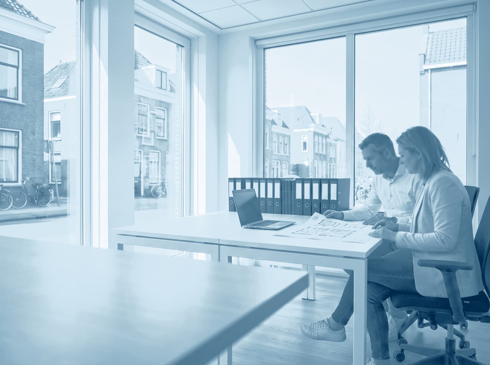 Twee collega's van een beheerkantoor bespreken een plattegrond aan een lichte werktafel