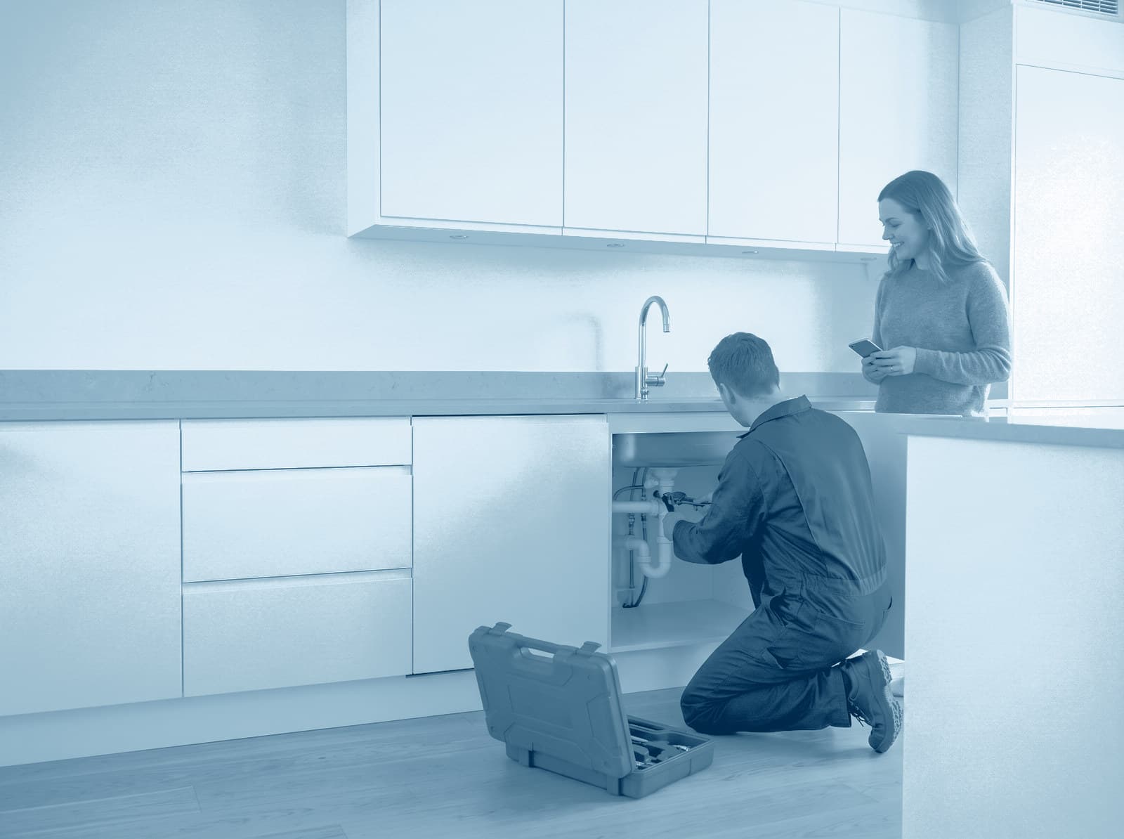 Loodgieter aan het werk onder het aanrecht terwijl de huurder toekijkt